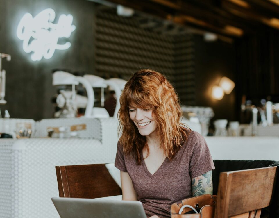 woman sitting on brown wooden chair while using silver laptop computer in room